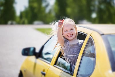 klein meisje op autovakantie zwaait uit het raam van een auto